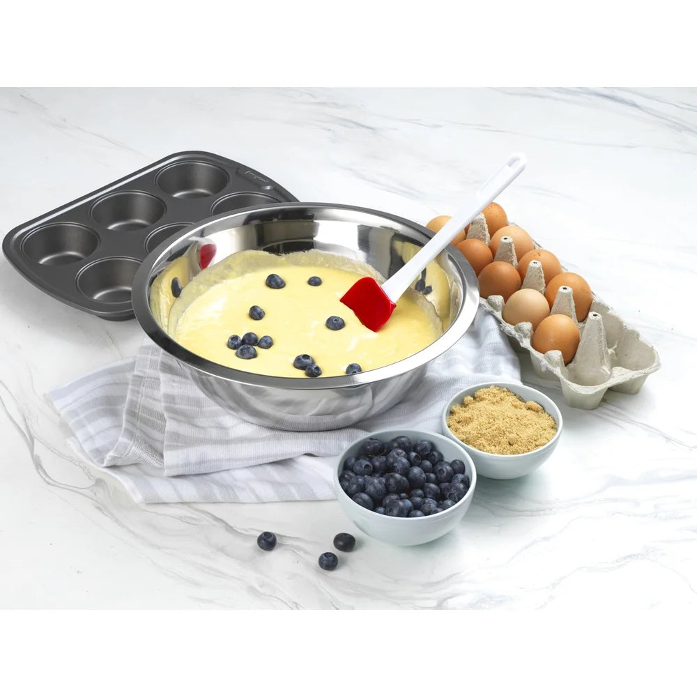 Baking setup with a mixing bowl, spatula, eggs, and ingredients on a white surface