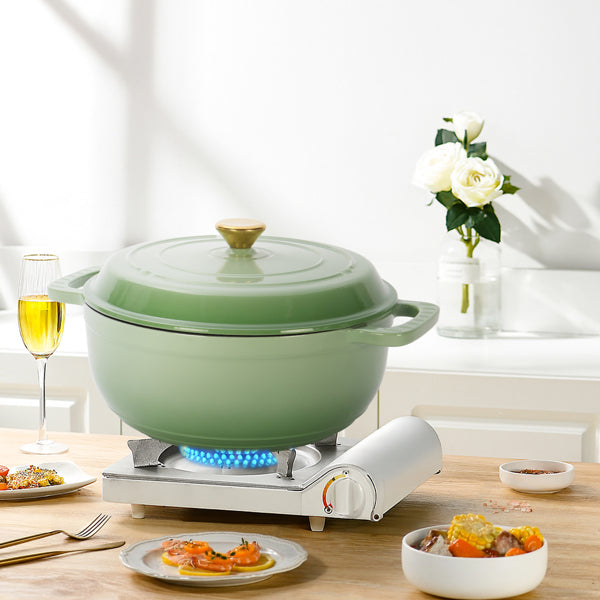 Green pot on a portable stove with plates of food and a glass of wine on a wooden table.