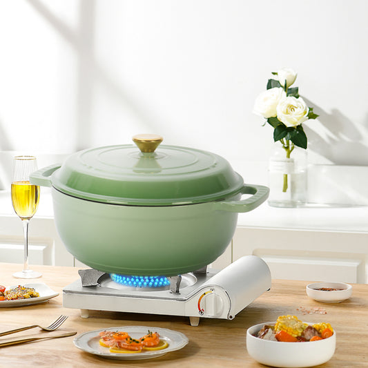 Green pot on a portable stove with plates of food and a glass of wine on a wooden table.